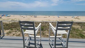 A beach view from a deck with white chairs, sandy beach, and clear sky.