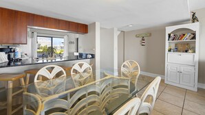 A modern kitchen with a glass dining table, wooden cabinets, and a view of the outdoors.