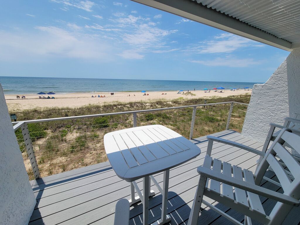 A balcony with a table and chairs overlooking a beach.