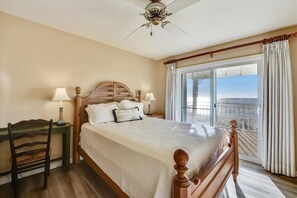 A bedroom with a large bed, a wooden headboard, two bedside lamps, a wooden chair, and a balcony with curtains. - CURRAN SEA IS THE PLACE TO BE! This beautifully designed home is the perfect family vacation home! (St. George Island)
