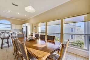 A spacious dining area with a large wooden table and wicker chairs, large windows offering a view of the outside, and a kitchen with white cabinets. - CURRAN SEA IS THE PLACE TO BE! This beautifully designed home is the perfect family vacation home! (St. George Island)