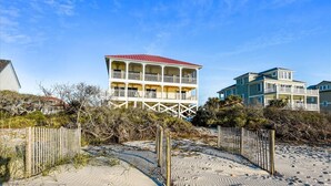 Une propriété située en bord de mer, avec un bâtiment à deux étages doté d’un balcon, entourée d’une plage de sable et de végétation.