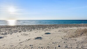 Une plage où l’on peut voir des empreintes de pas dans le sable, sous un ciel dégagé.