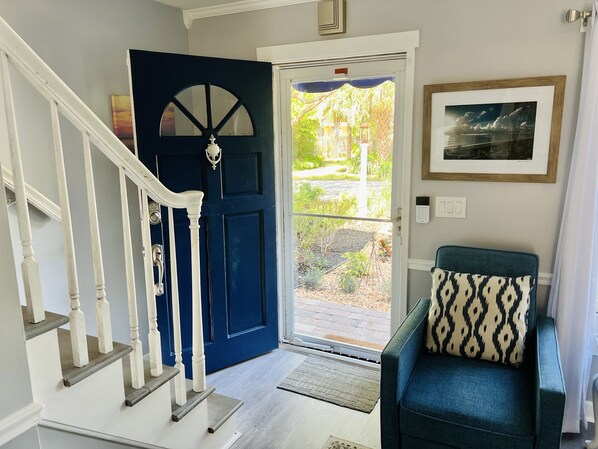 A staircase leading to a blue door with a glass panel, a green armchair with a patterned cushion, and a framed picture on the wall.