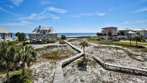 A beachfront property with multiple houses, a wooden boardwalk, and a clear view of the ocean.
