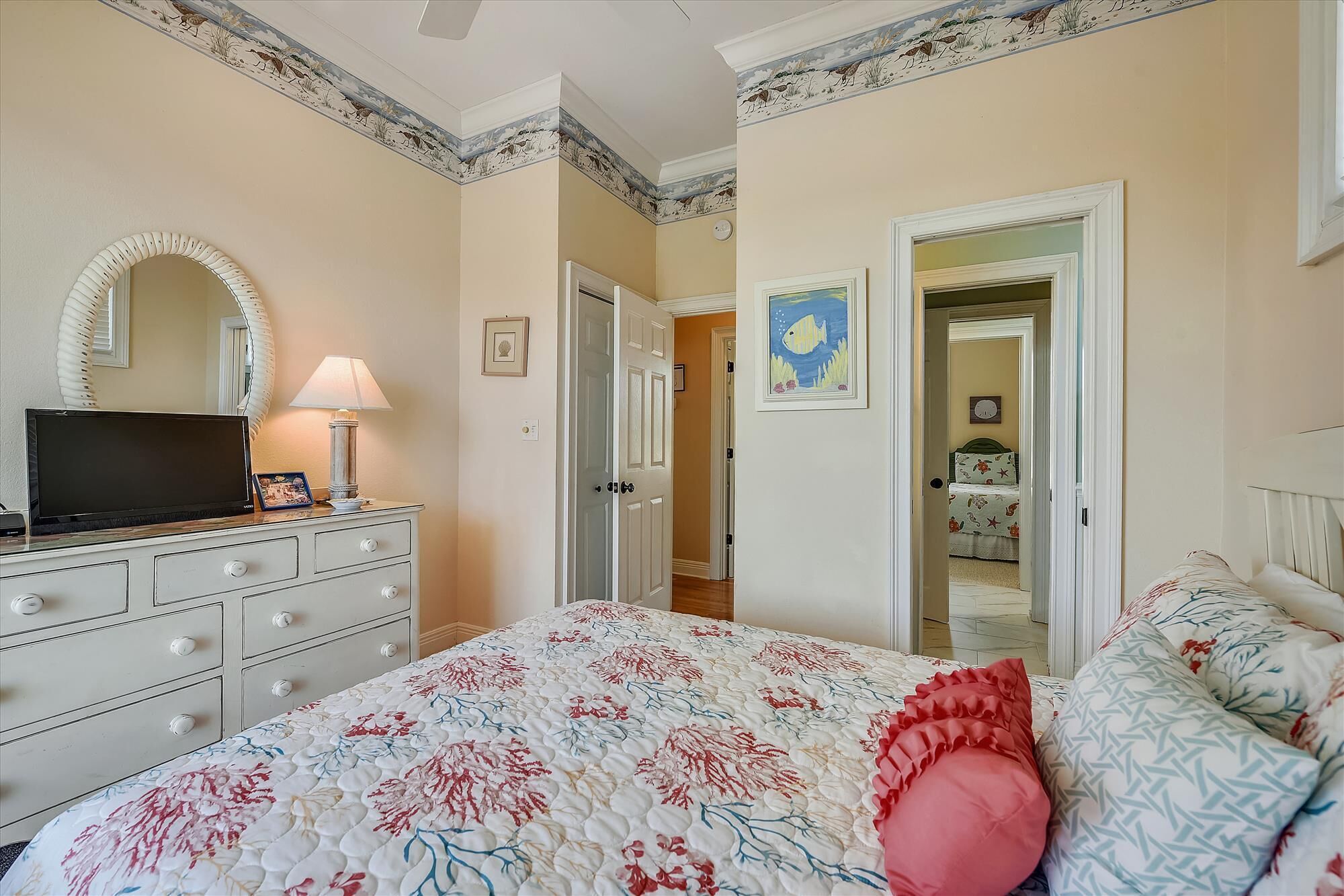 A bedroom with a bed, dresser, TV, and a door leading to another room.