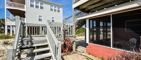 A beachfront property with a wooden deck, a red building with large windows, and a white building with balconies.