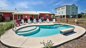 A swimming pool with lounge chairs, a red building, and a larger white building in the background.