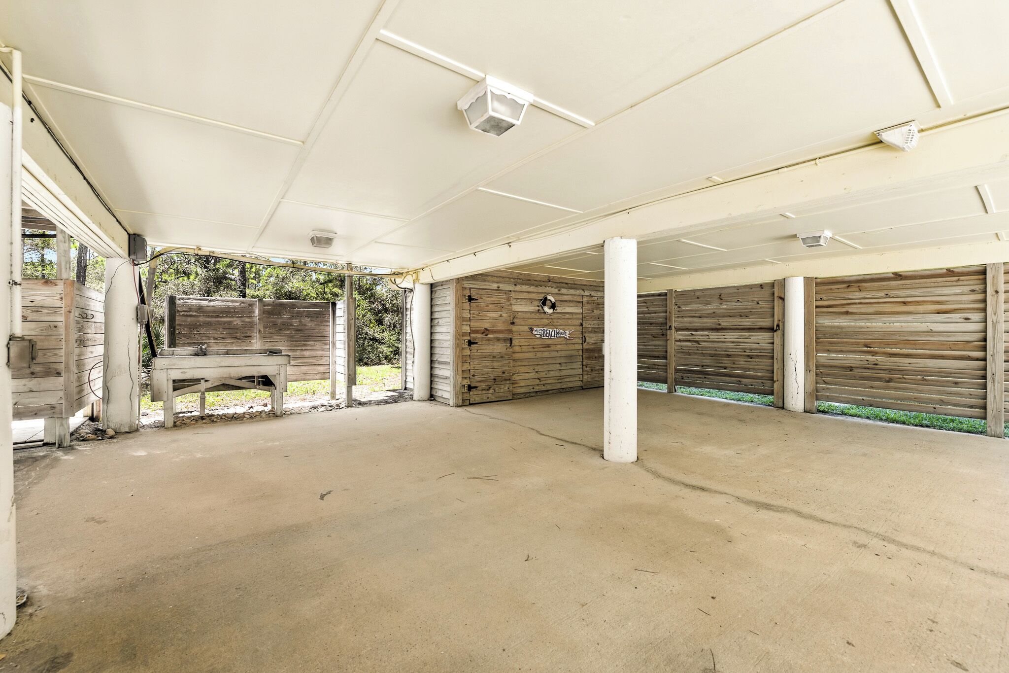 Un espace extérieur abrité, doté d’un sol en béton, de murs en bois et d’un banc.
