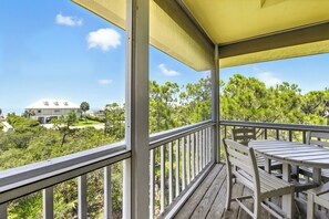 A covered outdoor deck with a table and chairs, overlooking a lush landscape with trees and a building in the background.
