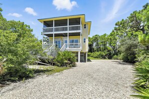 A two-story building with a balcony, surrounded by trees and a gravel driveway.