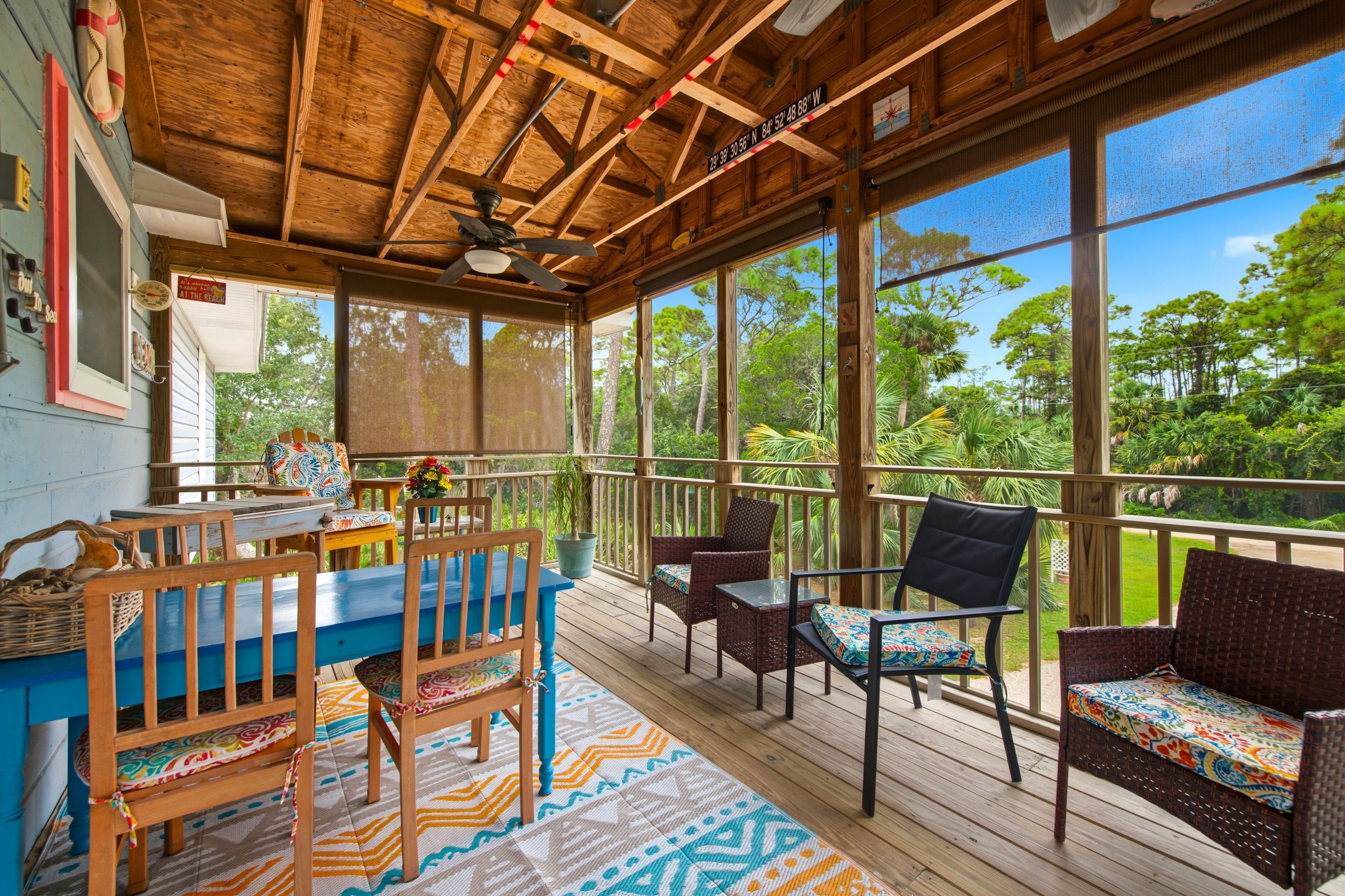 Un espacio al aire libre techado con mobiliario de madera, una mesa, sillas y vistas a zonas verdes.