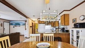 A modern kitchen with white cabinets, a wooden dining table, and a hanging light fixture.