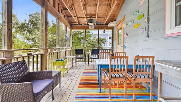 A covered outdoor deck with wooden furniture, a striped rug, and fish wall art.