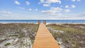 A wooden boardwalk leading to a beach with a clear sky.