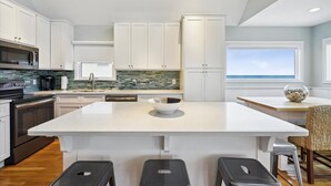 A modern kitchen with white cabinets, a large island, and a view of the ocean.