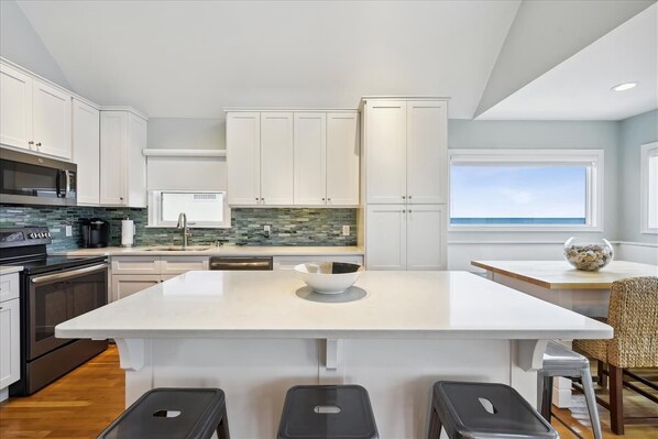 A modern kitchen with white cabinets, a large island, and a view of the ocean. - NATURAL SPLENDOR COMPLEMENTS contemporary style in this 2BR/2BA beach beauty. (St. George Island)