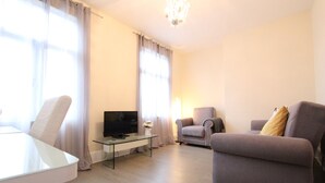A living room with a glass coffee table, a flat-screen TV, two armchairs, and a dining table. - Cosy One Bedroom Apartment- Marble Arch (London)