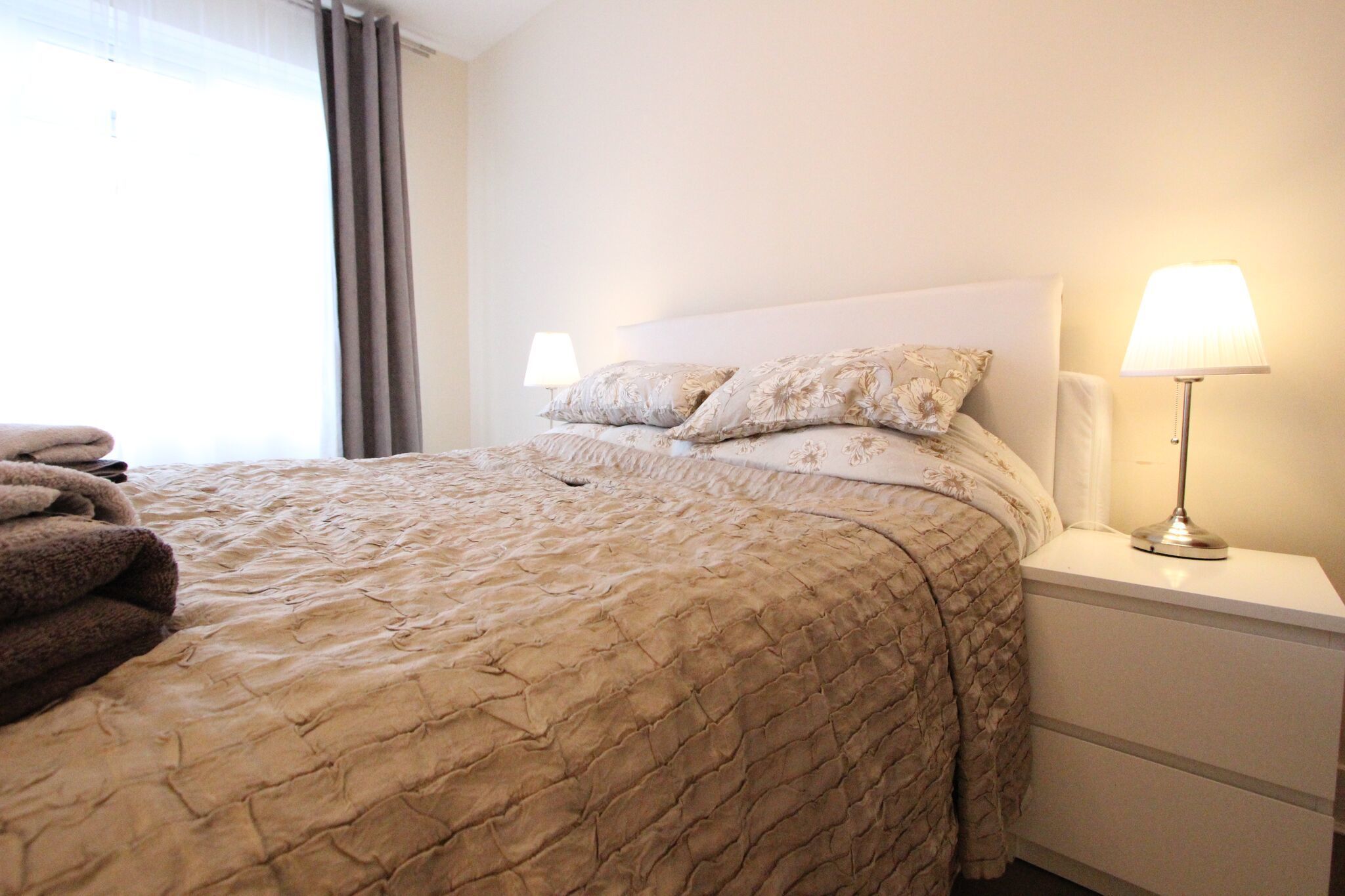 A neatly made bed with a quilted cover, two bedside lamps, and a folded towel on the nightstand.