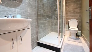 A modern bathroom with a glass-enclosed shower, a white sink, and a toilet. - Cosy One Bedroom Apartment- Marble Arch (London)