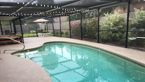 A swimming pool with a covered patio area, a lounge chair, and a small table.