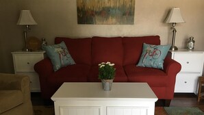 A living room with a red sofa, two side tables with lamps, a white coffee table with a plant, and a colorful rug.
