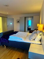 Habitación de hotel con cama, lámpara de noche y puerta que da a otra habitación.