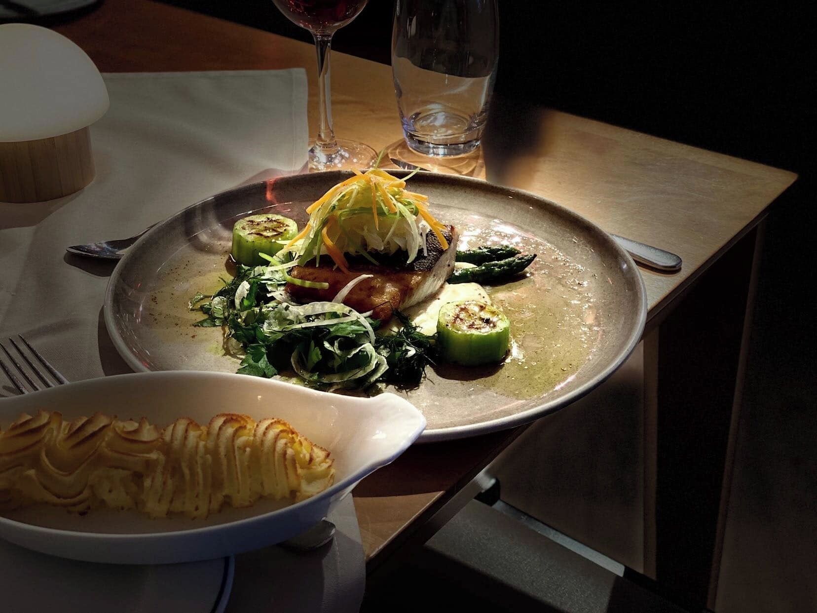 A dining table with a plate of food, a glass of water, and a glass of red wine.