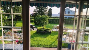 A view from a conservatory with a wooden deck, outdoor seating, and a well-maintained lawn. - Skaslien Gjestgiveri (Grue)