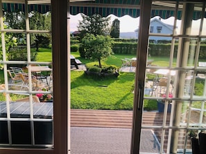 A view from a conservatory with a wooden deck, outdoor seating, and a well-maintained lawn. - Skaslien Gjestgiveri (Grue)