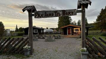 A wooden sign with the text 'FRA LORD TIL BORD' and a gravel path leading to a building with a covered porch.
