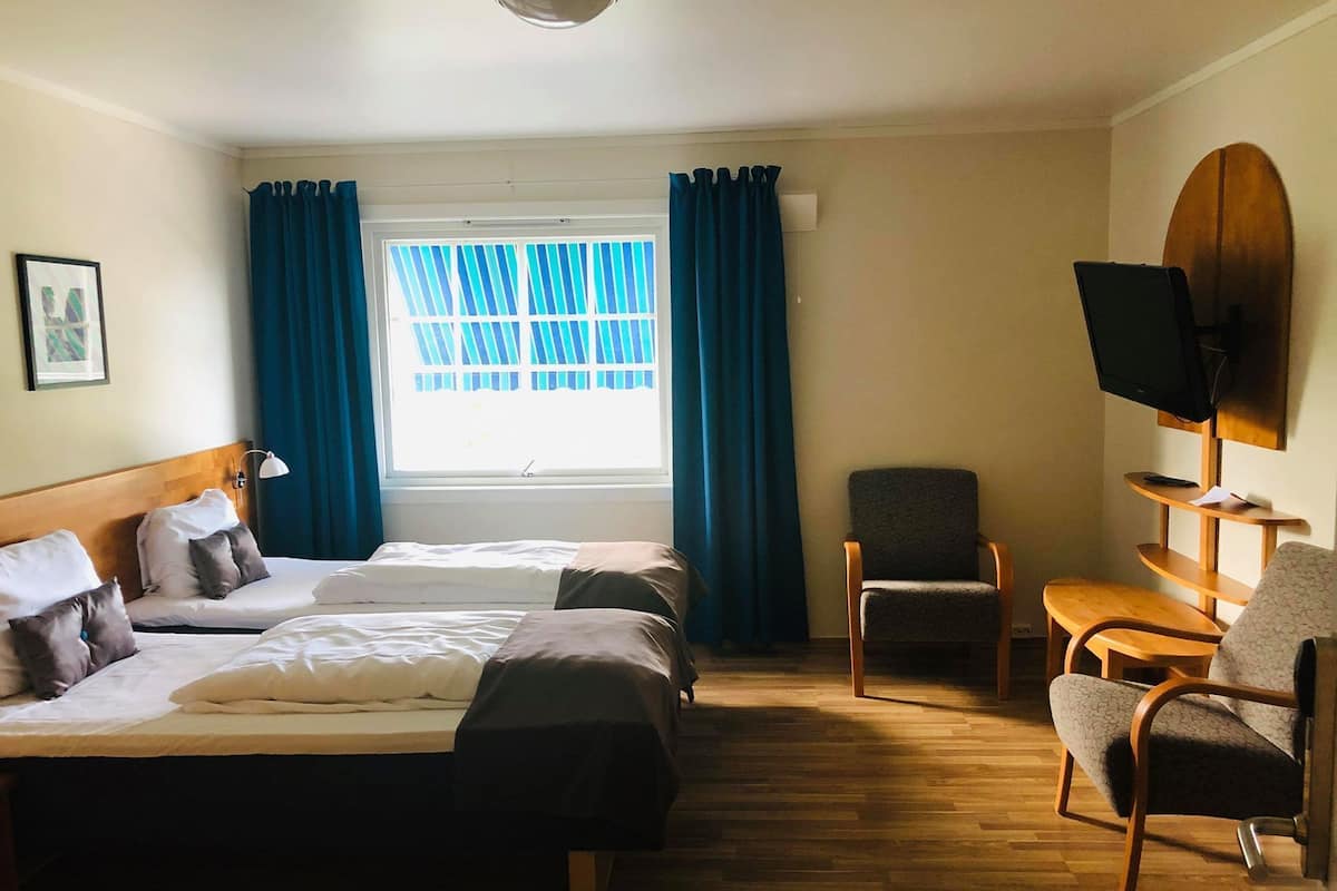 A hotel room with two beds, a TV, a chair, and a window with curtains.