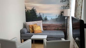 Un soggiorno moderno con un divano, due poltrone, un tavolino da caffè, una televisione a schermo piatto e un grande murale.
