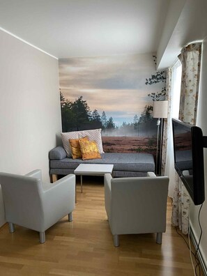 A modern living room with a sofa, two armchairs, a coffee table, a flat-screen TV, and a large wall mural. - Skaslien Gjestgiveri (Grue)
