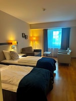 Quarto de hotel com duas camas, uma escrivaninha, uma cadeira e um sofá.