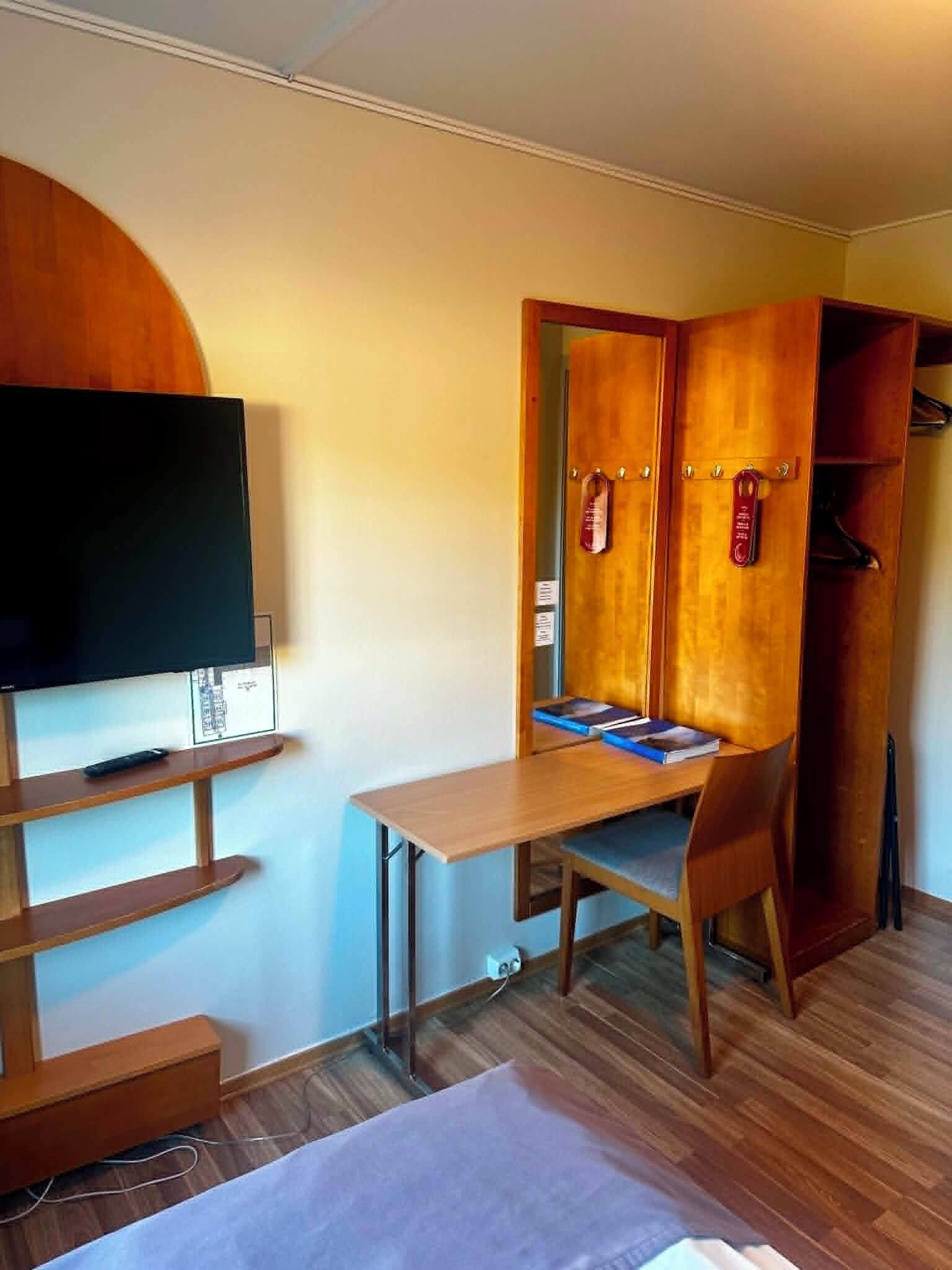 A room with a bed, a desk with a chair, a television, and a wardrobe.