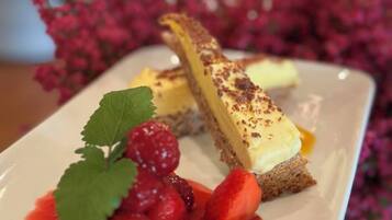 Een taartbord met een stuk cheesecake op een cracker, versierd met een aardbei en een blaadje, met rode saus en bessen, voor een achtergrond met roze bloemen en kaarsen.