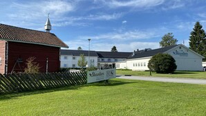 A building with a sign reading 'Skaslien Gjestgiveri,' a red barn, and a white building with a sloped roof. - Skaslien Gjestgiveri (Grue)