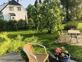 Un patio con mobiliario exterior, una planta en maceta y una casa al fondo.