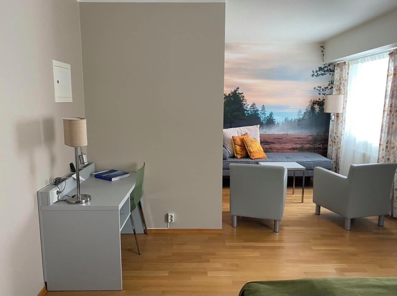 A modern room with a desk, two chairs, a sofa, and a large window with a view of trees.