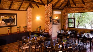 A restaurant with brick walls, wooden beams, and large windows. Tables are set with plates, glasses, and cutlery. - Elgro River Lodge (Potchefstroom)