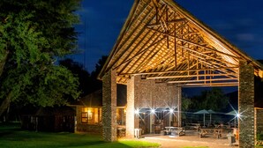 A large, open pavilion with a wooden roof and brick walls, featuring outdoor seating and a well-lit patio area. - Elgro River Lodge (Potchefstroom)
