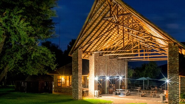 A large, open pavilion with a wooden roof and brick walls, featuring outdoor seating and a well-lit patio area. - Elgro River Lodge (Potchefstroom)