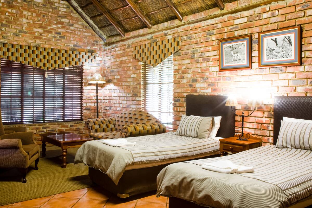 A room with two beds, a sofa, a small table, and a brick wall with pictures.