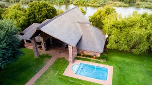 A lodge with a thatched roof, a swimming pool, and a view of a lake. - Elgro River Lodge (Potchefstroom)