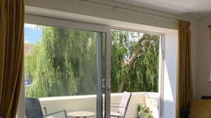 Un salon moderne avec un canapé, une table à manger et des chaises. Une porte-fenêtre coulissante donne sur un balcon extérieur d’où l’on peut admirer des arbres et un immeuble.