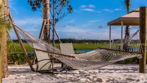 A hammock on a sandy beach with a clear sky and a distant view of a water body. - H-Gated Resort-5 miles to Disney-2 FREE Water Park (Osceola County)