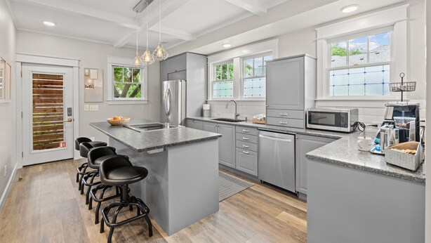 A modern kitchen with grey cabinetry, a central island with bar stools, stainless steel appliances, and large windows. - PRISTINE PROPERTY IN PRIME LOCATION — CHARMING ☆ SAFE ☆ WALK TO EVERYTHING (Nashville)