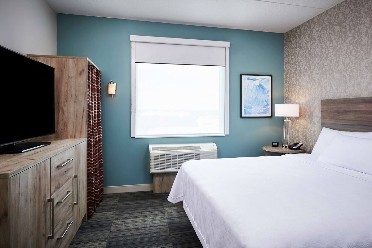 A hotel room with a bed, a TV, a heater, a lamp, and a picture on the wall.