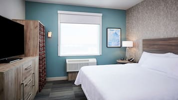 Ett hotellrum med en säng, en tv, en värmare, en lampa och en tavla på väggen.